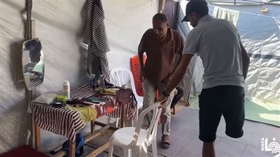 حلاق فلسطيني يواجه الاحتلال بالإصرار على ممارسة عمله داخل خيمة بعد بتر قدمه.. فيديو
